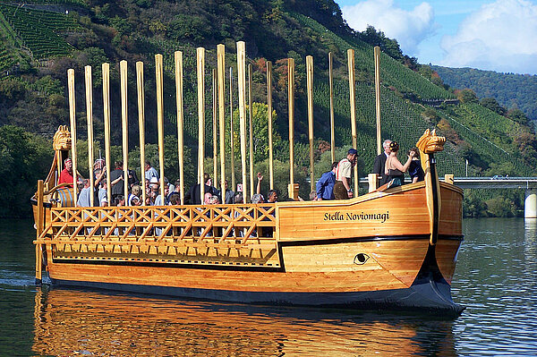 Holzschiff, viele Personen an Bord, die Ruder sind an beiden Seiten nach oben gestellt