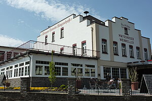 Das historische Gebäude der "Winzergenossenschaft Mayschoß-Altenahr" heute, auf der Frontfassade die Beschriftung "Mayschoßer Weinkeller", davor eine Außenterrasse.